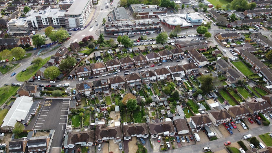 An aerial view of a suburban residential area showing multiple back gardens separated by fences, featuring a variety of landscaping styles. The gardens include lush green lawns with neatly trimmed gra